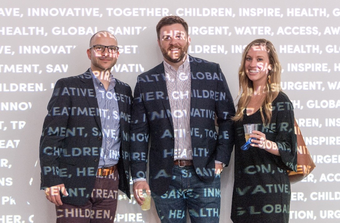 Two men and a woman covered in a wall projection of words like health, innovative, solutions