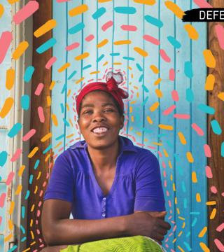 Zambian woman sitting and smiling in front of a bright blue door with blue, pink, and orange paint brush strokes encircling her