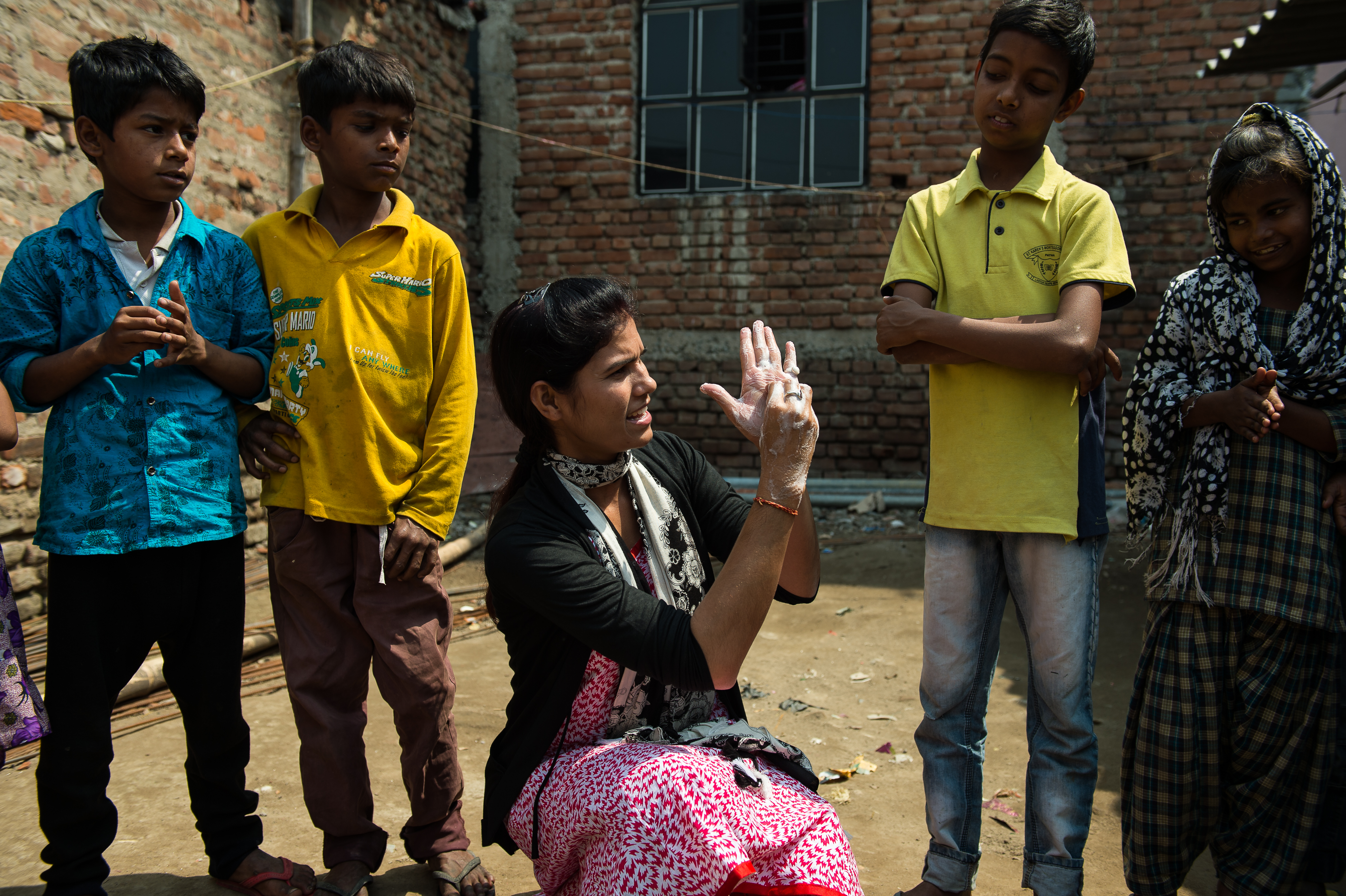 Female community health volunteer in India demonstrates handwashing to a group of children.