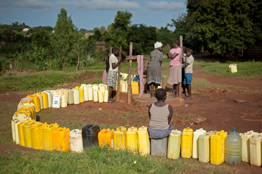 Long row of bright yellow jugs and a group of women at a water spigot