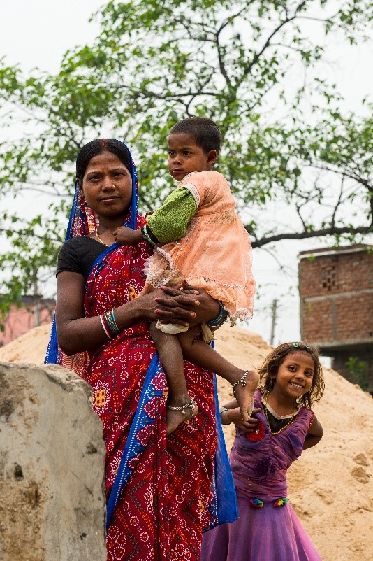 Mother holds her daughter, and a smiling girl peeks from behind 
