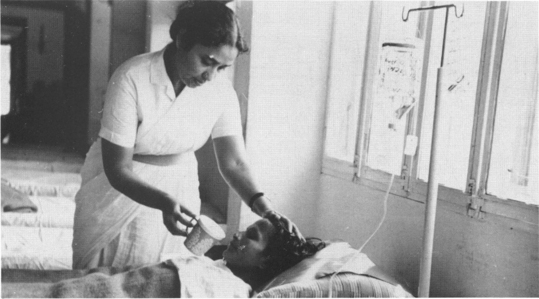 Black and white photo of a female nurse giving oral therapy to a patient in a hospital
