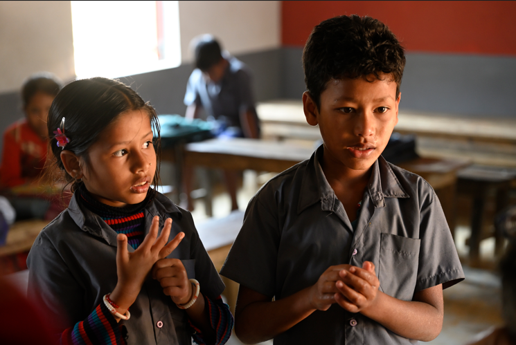 Two Indian students, a boy and a girl, in a classroom with school desks behind them
