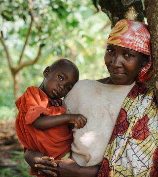 A woman in Uganda leaning against a tree holding a boy