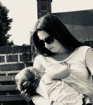 Black and white photo of a woman in sunglasses looking down and breastfeeding her baby