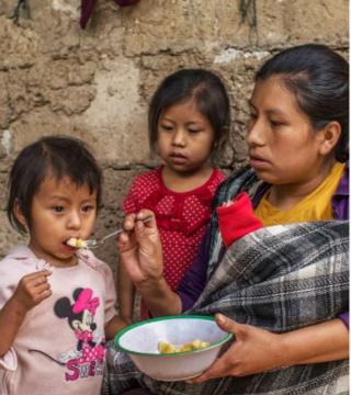 Mother in Guatemala feeds her daughter mashed bananas as another child looks on