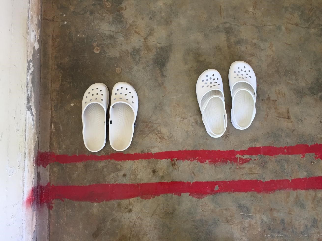 Two pairs of white shoes on the floor behind a double line of red paint
