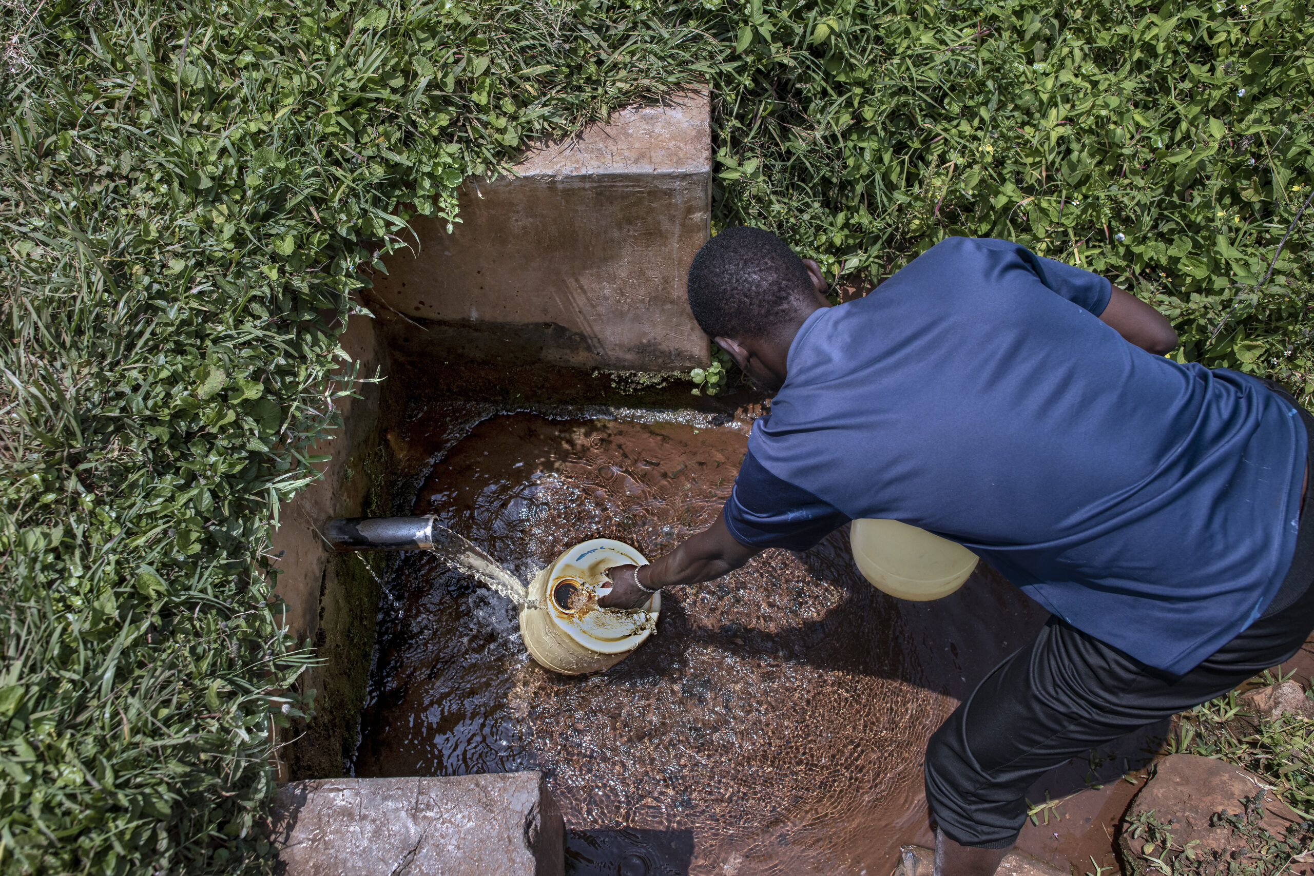 A man fills a water container from an outdoor faucet.
